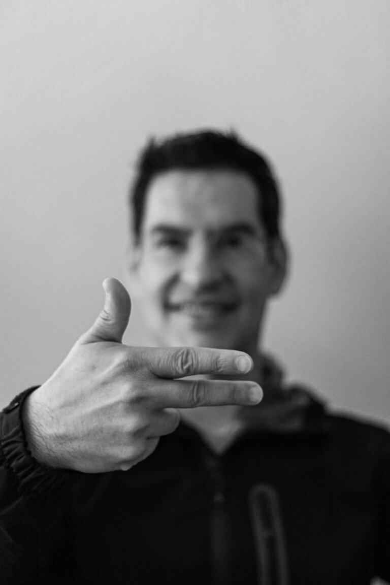 Black and white portrait of a man smiling and making a hand gesture.