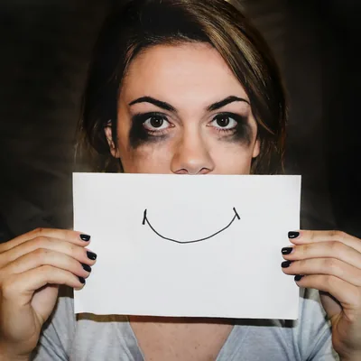 Une femme tient devant son visage une feuille où un sourire est dessiné